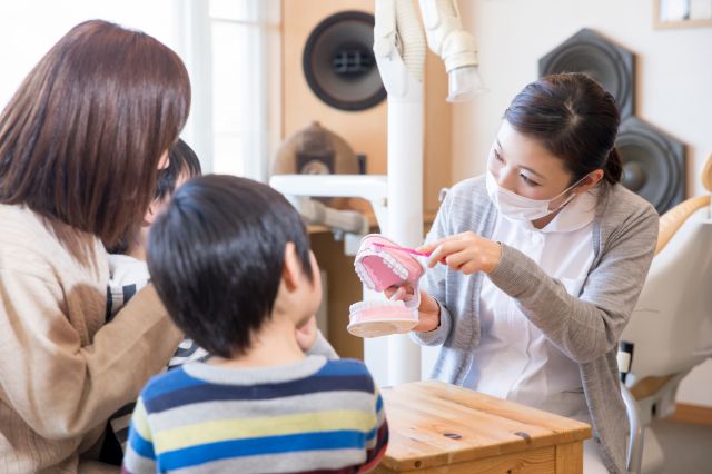 子どもと母親に歯ブラシの仕方を教える女性歯科スタッフ